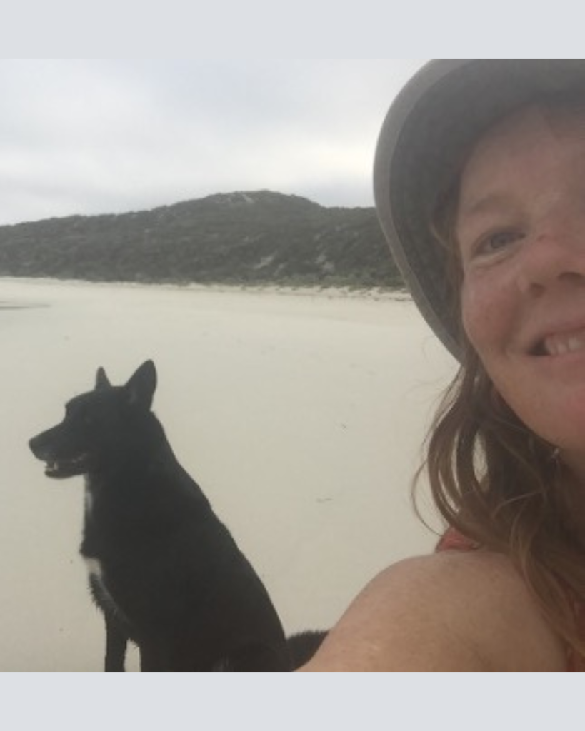 Liluella and her dog at a beach on an overcast day with land and ocean behind them.
