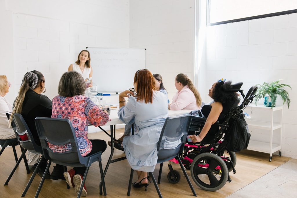 A group of people with disability sitting around a table listening to a presenter.