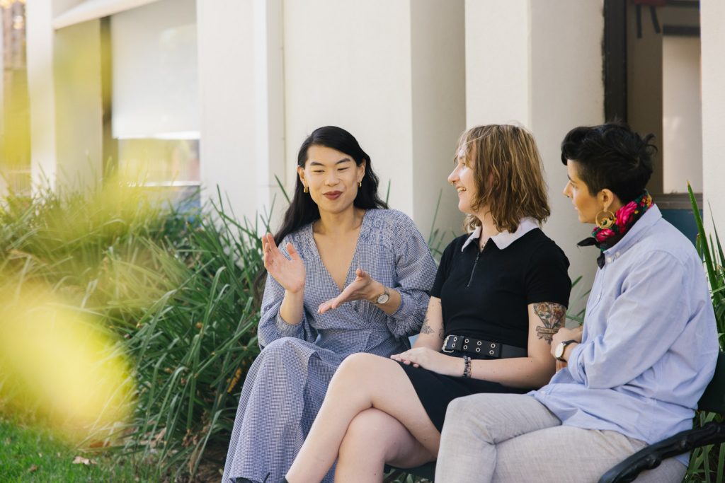 Three people sit on a park bench talking.